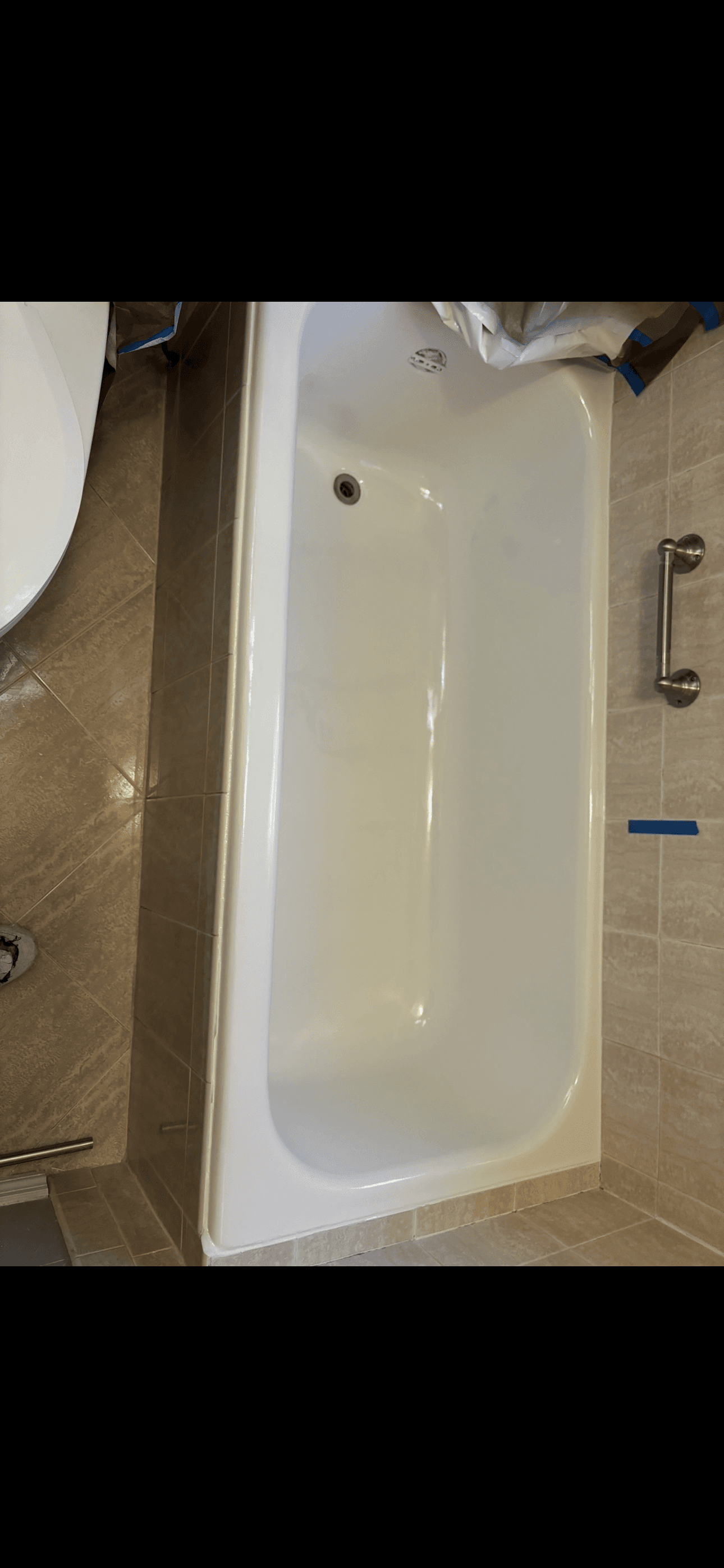 A clean white bathtub set against beige tiled walls and floor with a metal grab bar.