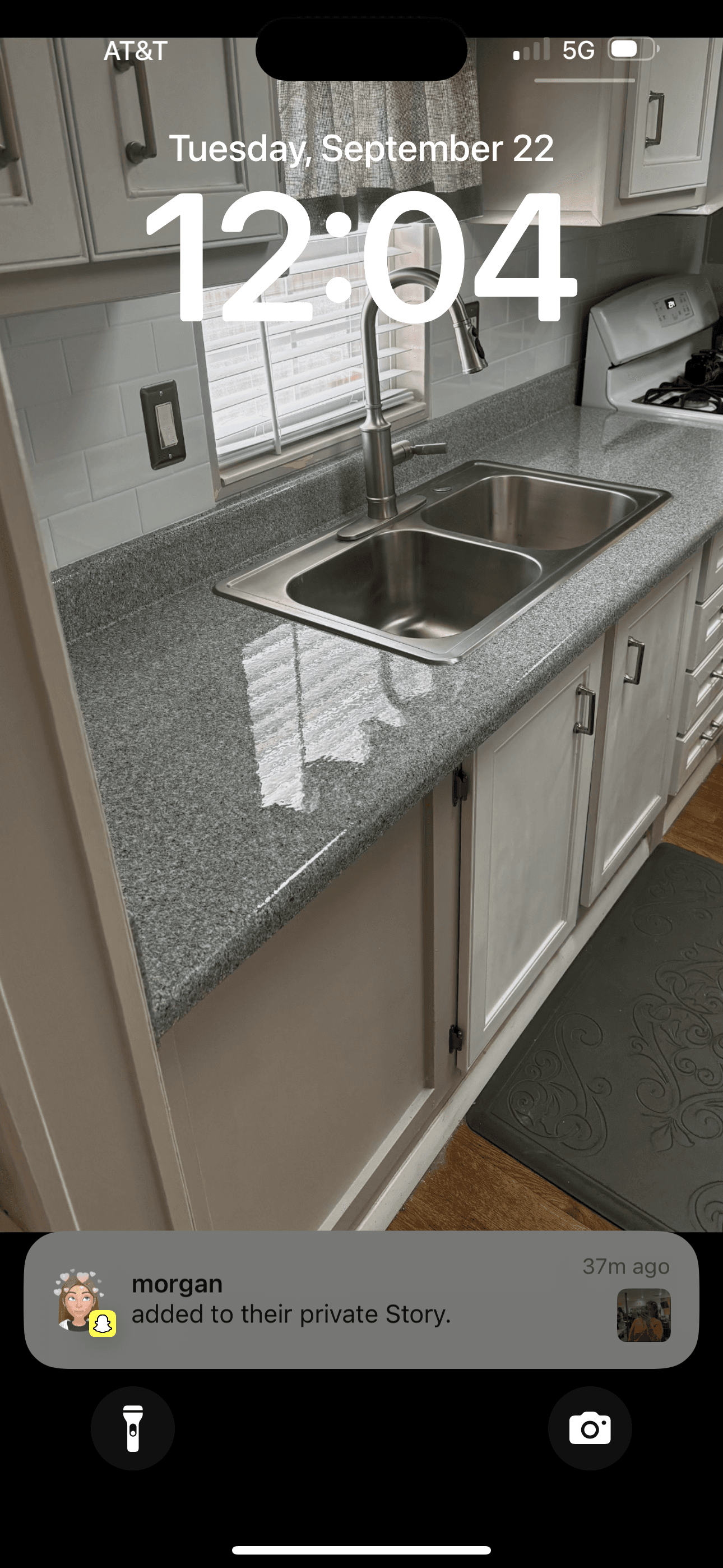 iPhone lock screen showing 12:04 and a notification over a kitchen sink and granite countertop.