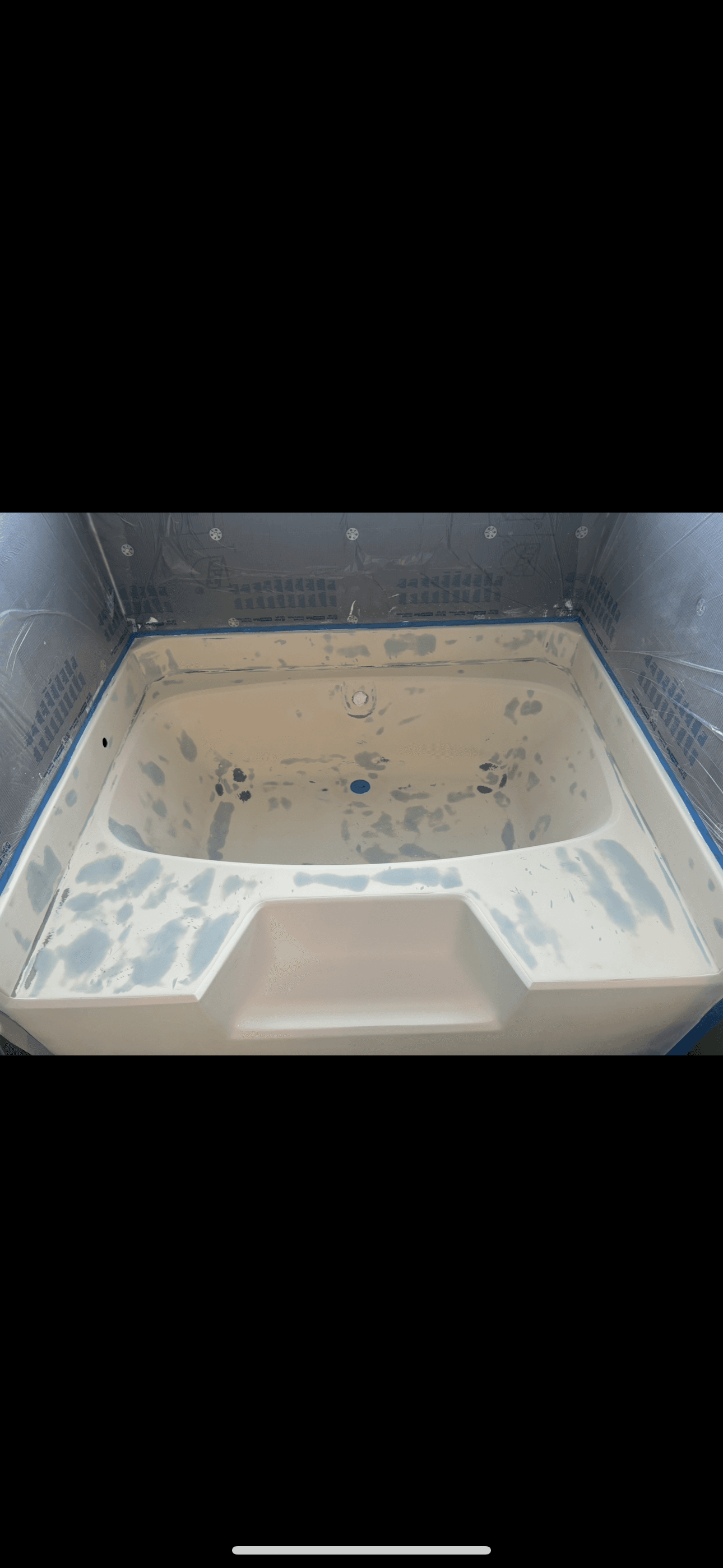 White bathtub being refinished with blue filler patches, surrounded by protective plastic and tape.