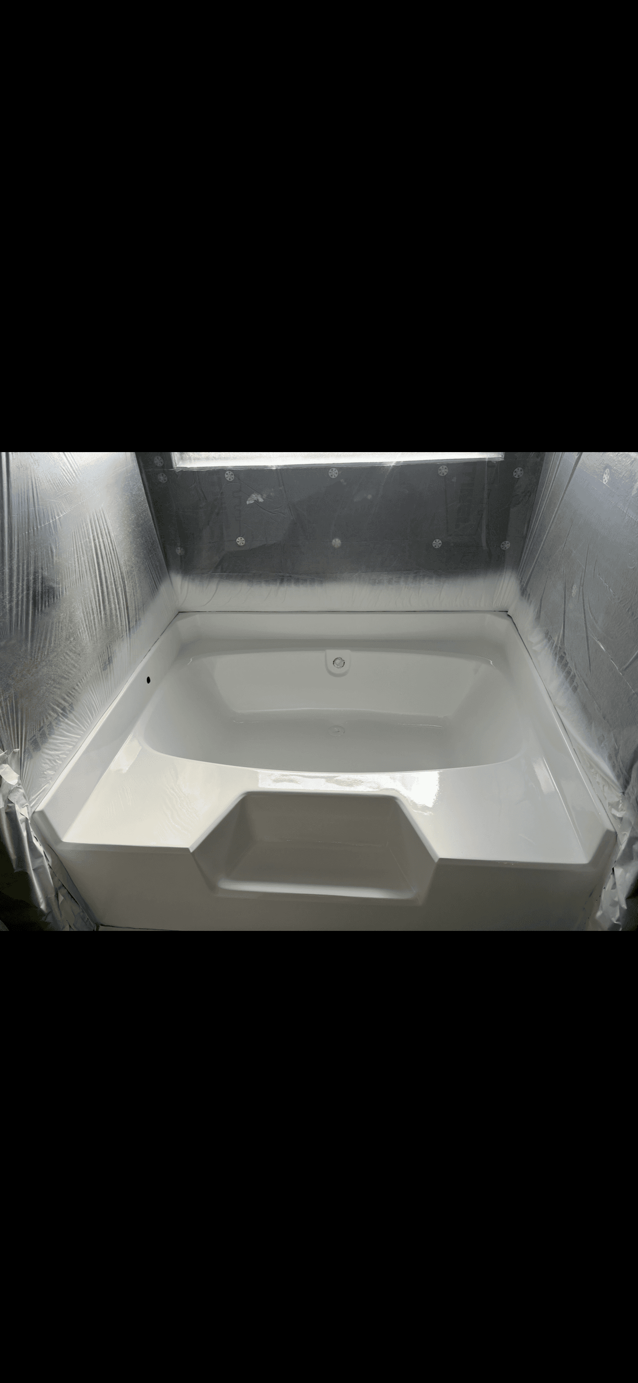 Newly glazed white bathtub in a bathroom under renovation with plastic-covered walls.