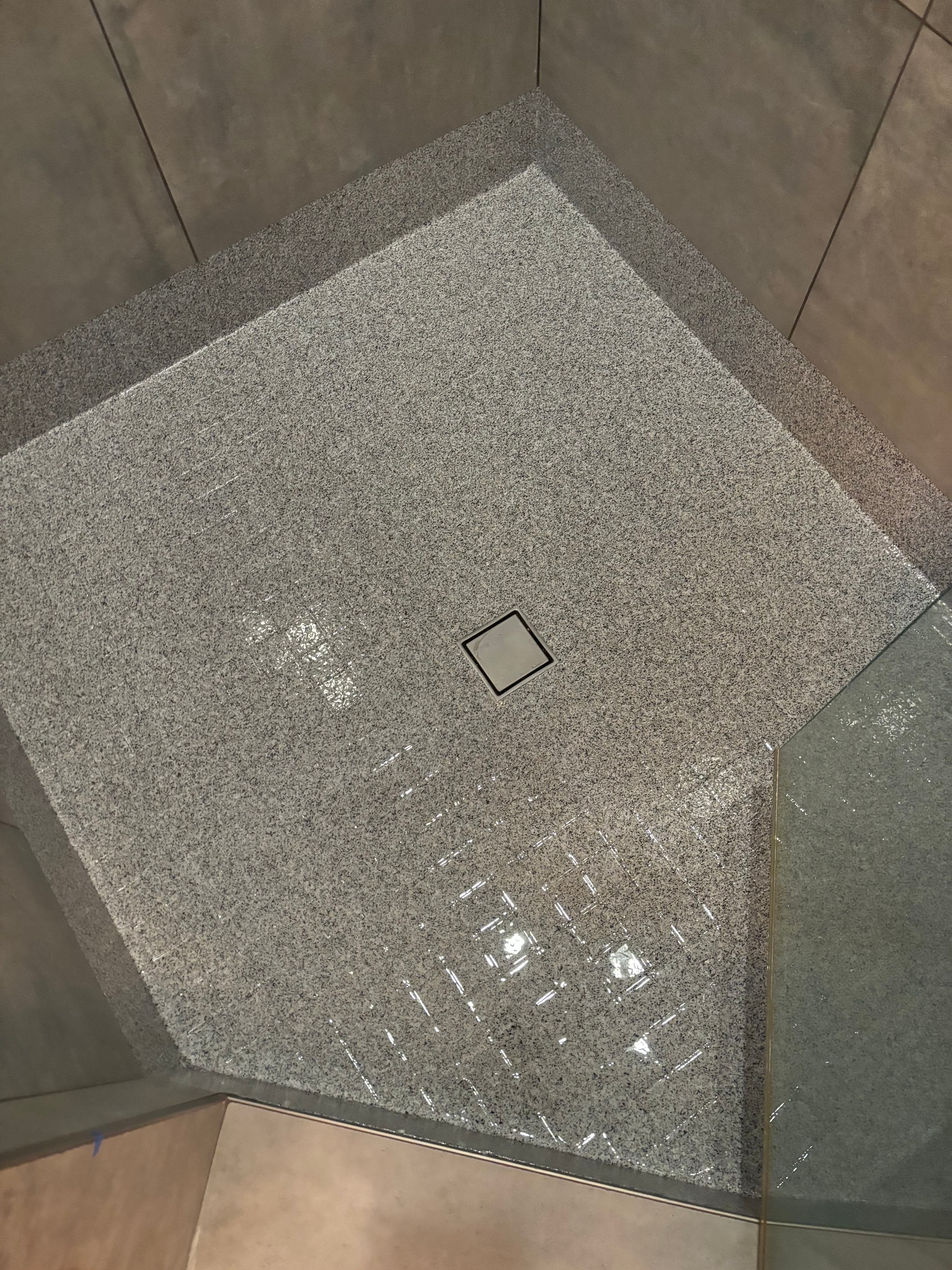 Wet grey speckled shower floor with a square drain and reflections from overhead lights.