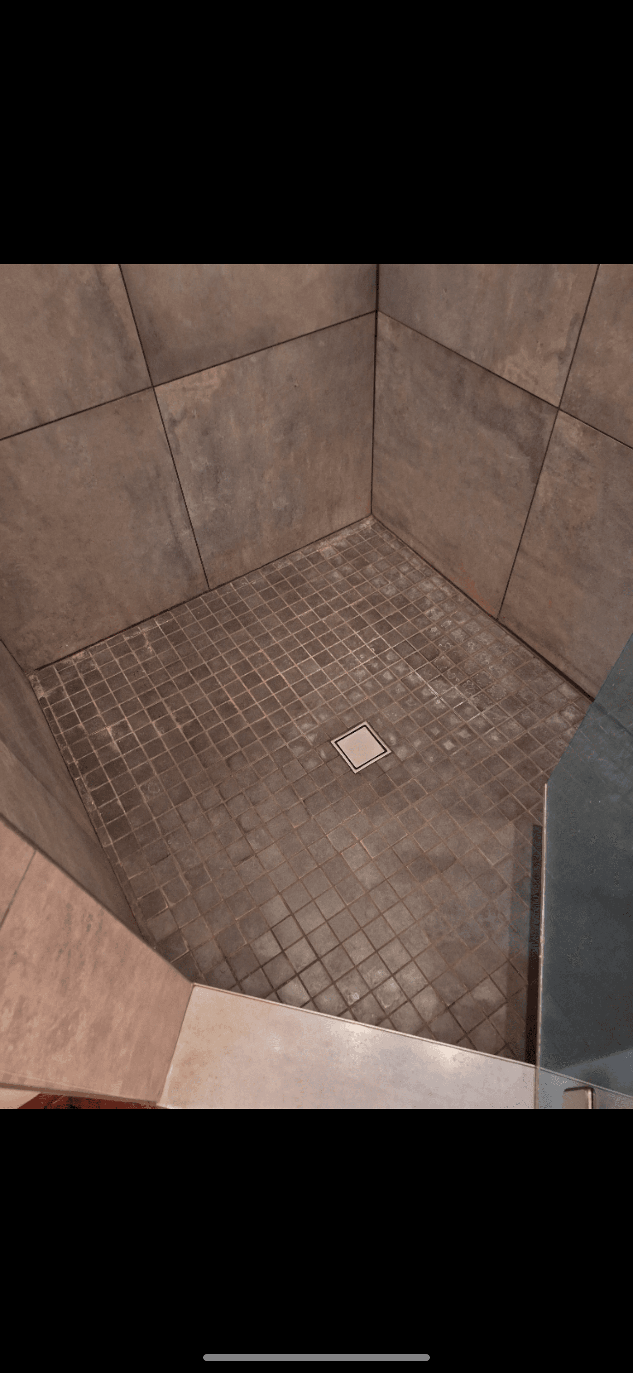 Modern walk-in shower with large grey wall tiles and small square floor tiles with central drain.